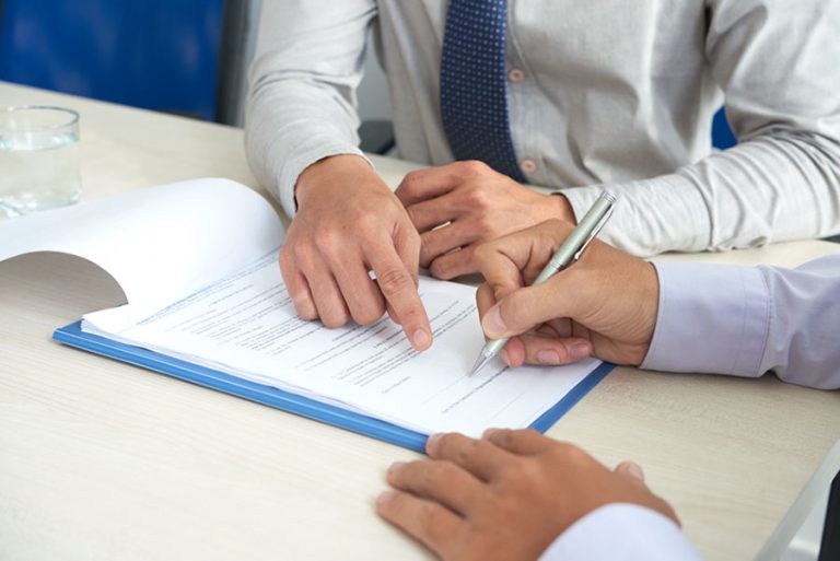 Las manos de dos personas, una firmando el contrato de arras y la otra señalandolo