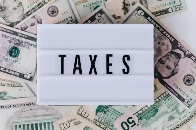 Fondo con dólares y cuadrícula blanca que dice TAXES (impuestos).