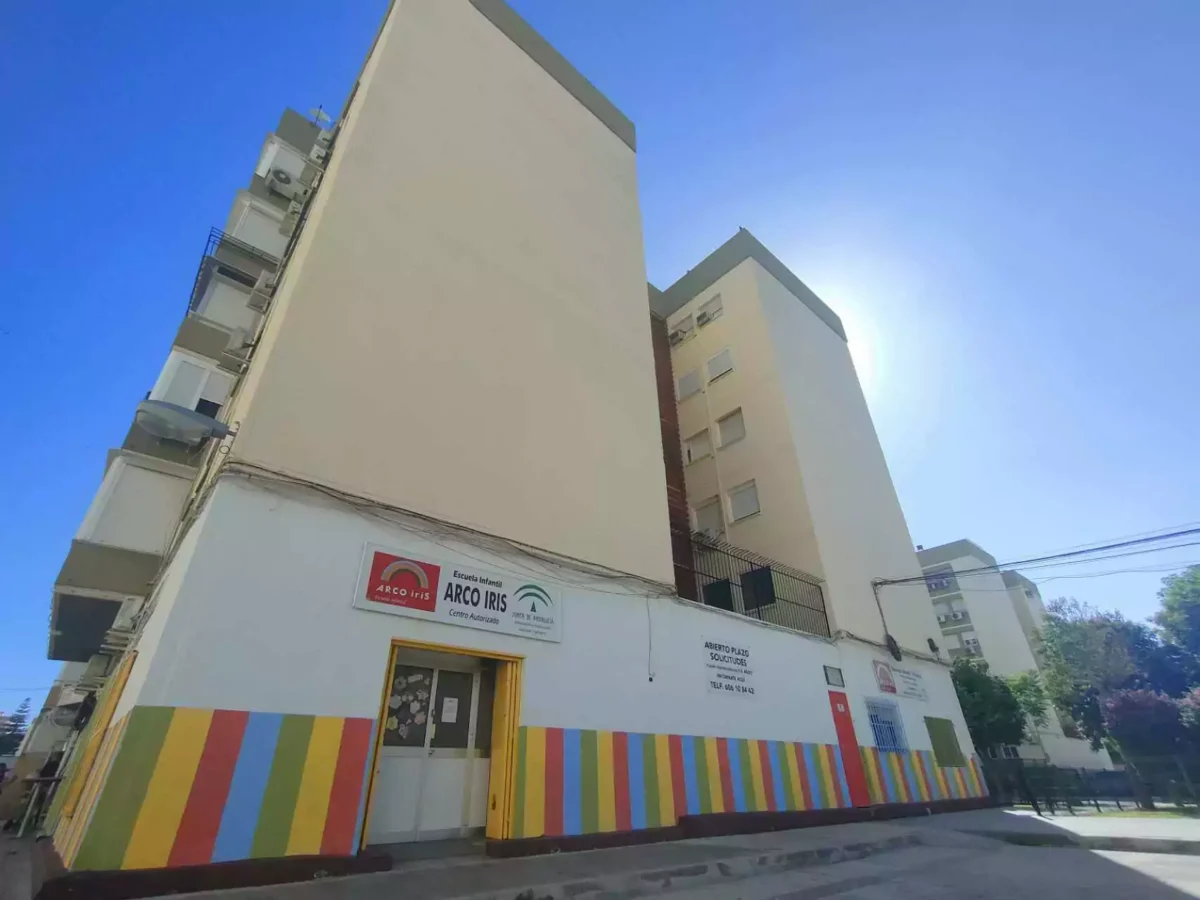 Entrada de la Escuela Infantil Arco Iris en el barrio de Los Príncipes Sevilla, con edificios y cielo despejado.