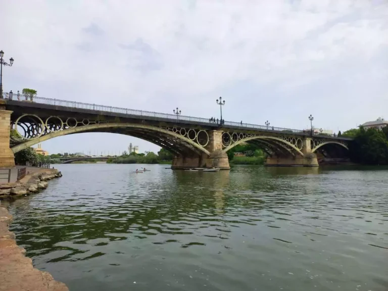 Puente de hierro con círculos de decoración y el río Guadalquivor