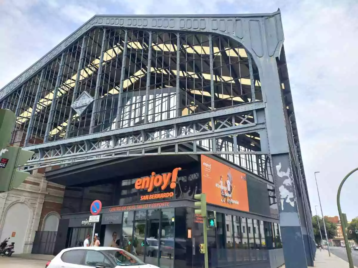 Edificio de cristal y hierro de dos plantas. Tiene un cartel en naranja con el nombre Enjoy!