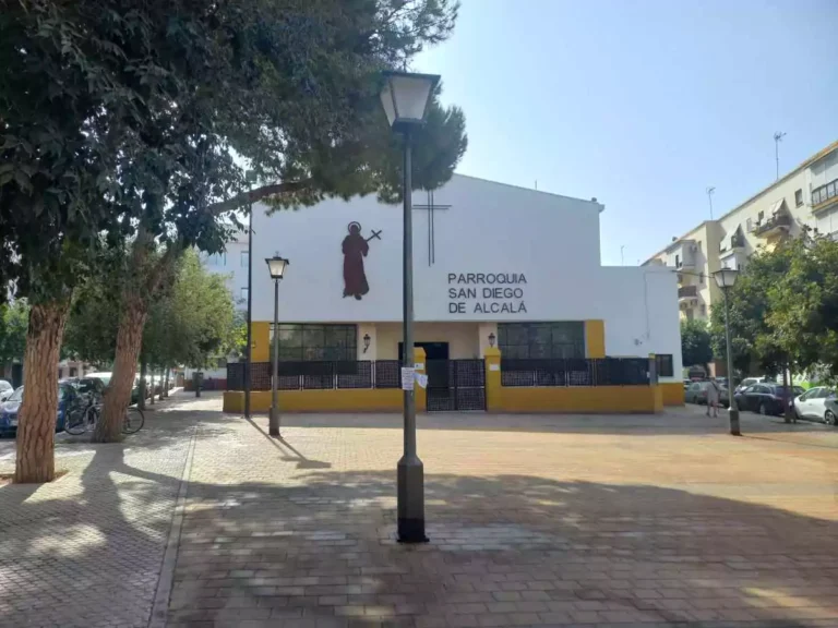 Plaza con una parroquia con fachada blanca y árboles alrededor