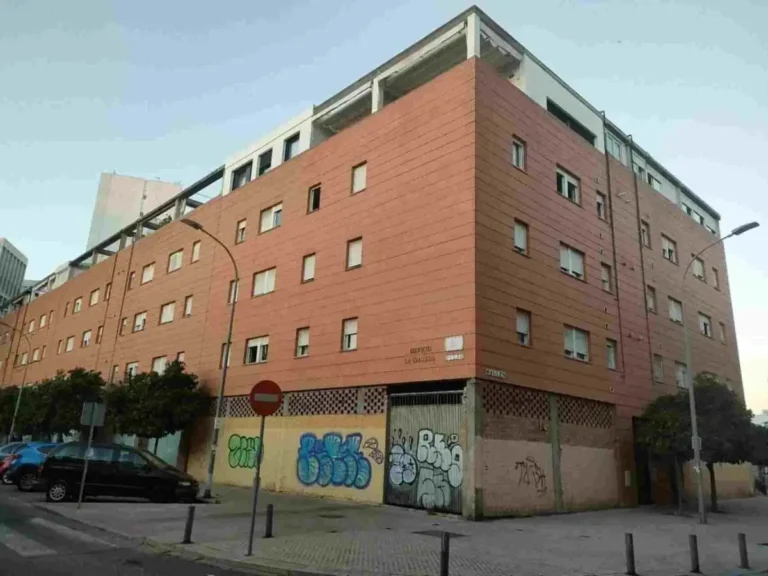 Edificio grande de ladrillo que hace esquina y que tiene grafitis en la parte baja