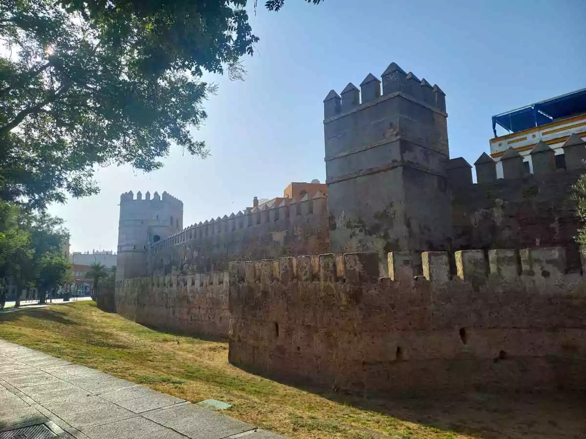 Muralla de piedra con varias torres y con un cesped justo delante