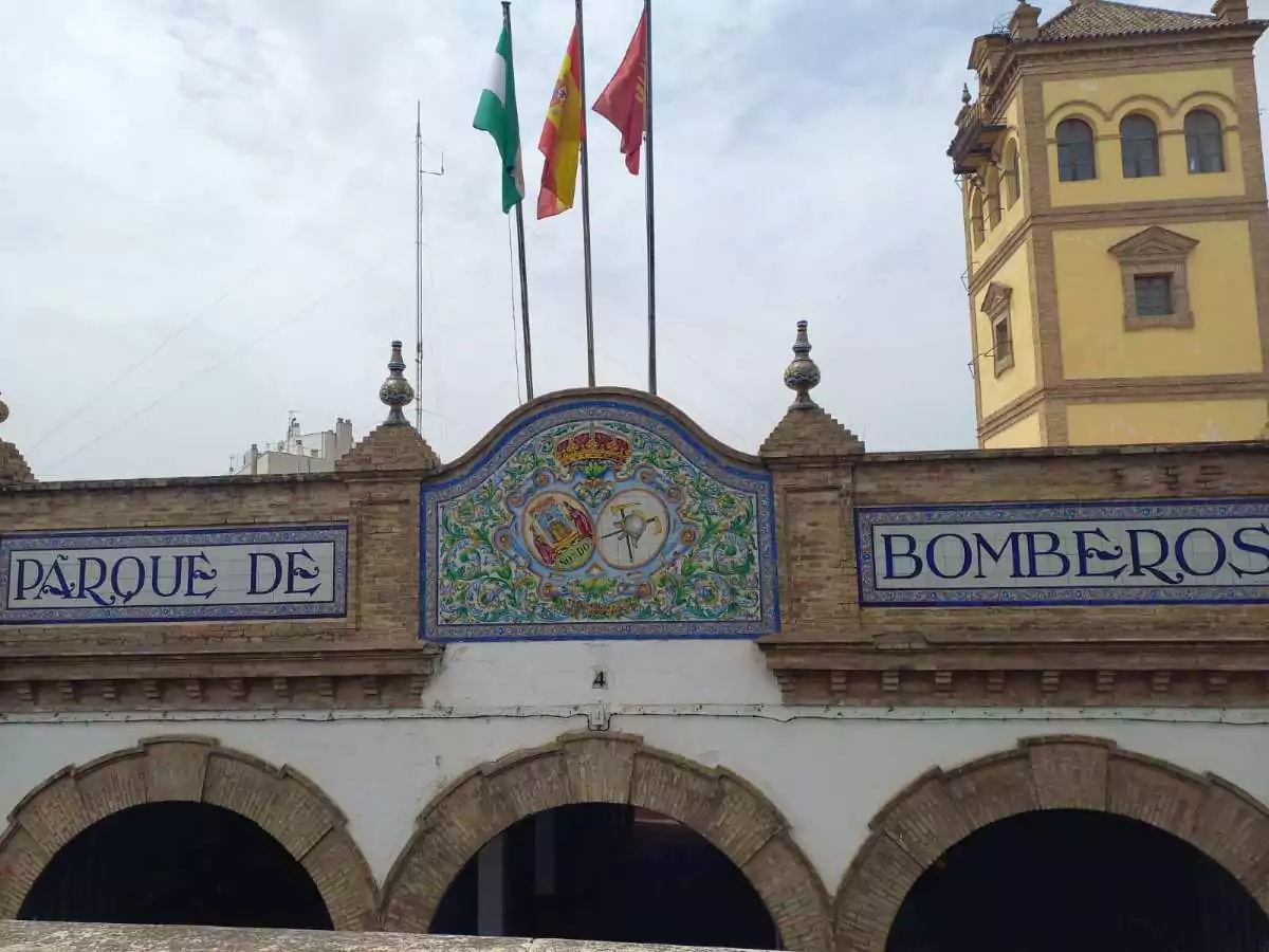 Edificio blanco, con tres entradas, y un cartel formado por azulejos que pone “Parque de Bomberos”.