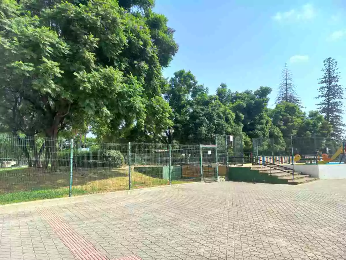 Zona arbolada con parque infantil vallado que limita con la calle