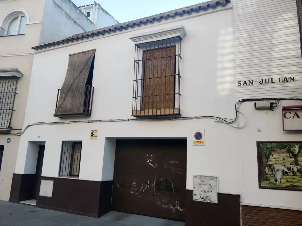 Fachada blanca de una casa en el barrio de San Julián, se aprecia una puerta de cochera marrón.